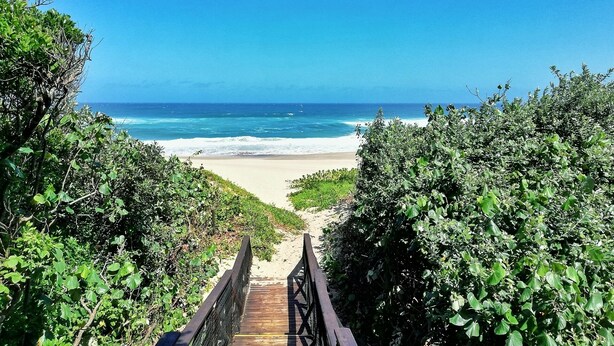 A wooden boardwalk leading to a beach with clear blue water and a sandy shore. - Caribbean Estate Deluxe (Port Edward)