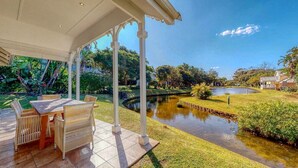 A covered patio with a dining table and chairs, a small pond, and lush greenery. - Caribbean Estate Deluxe (Port Edward)