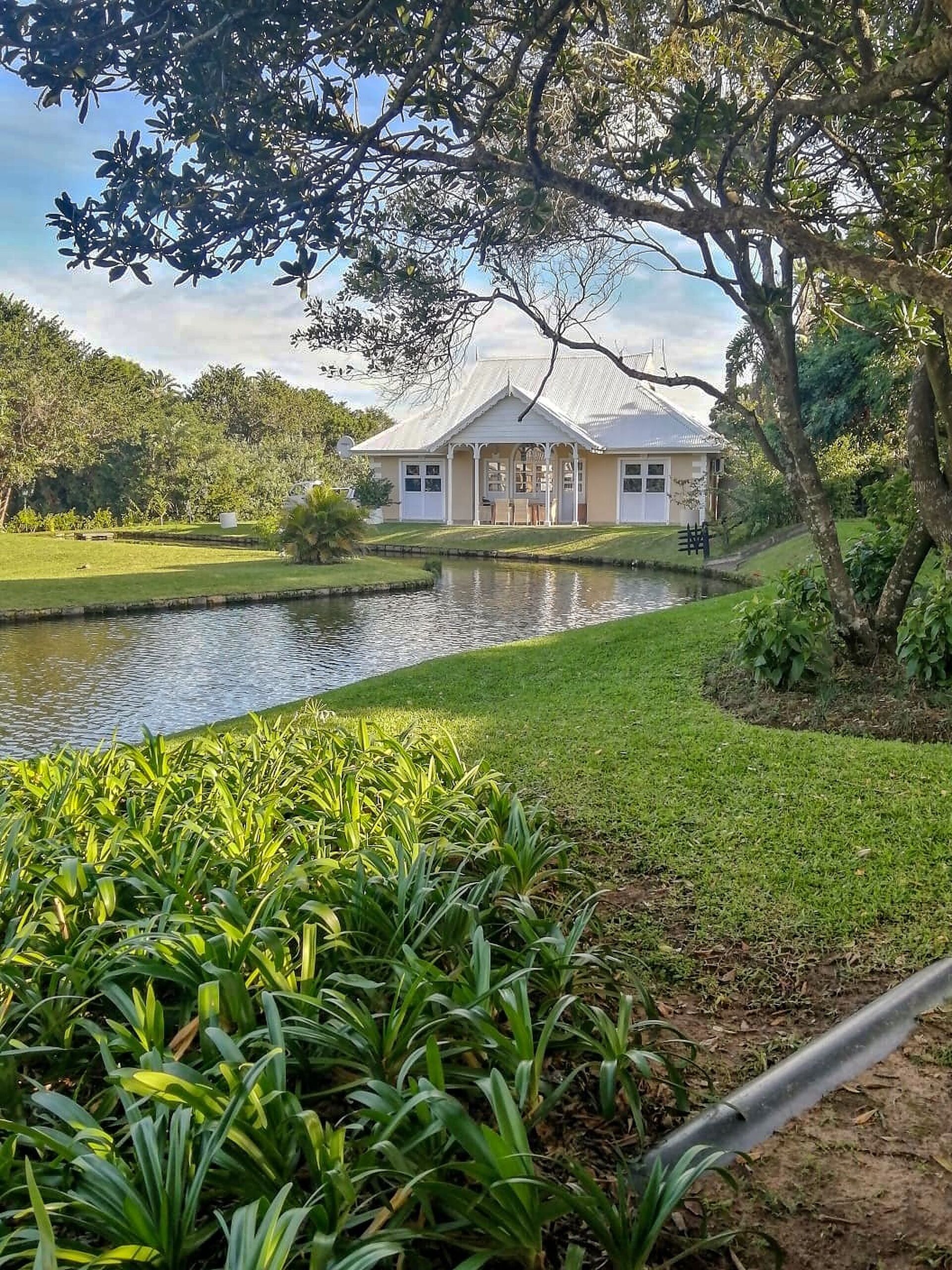 Ein Haus mit Teich im Vordergrund, umgeben von üppiger Vegetation.