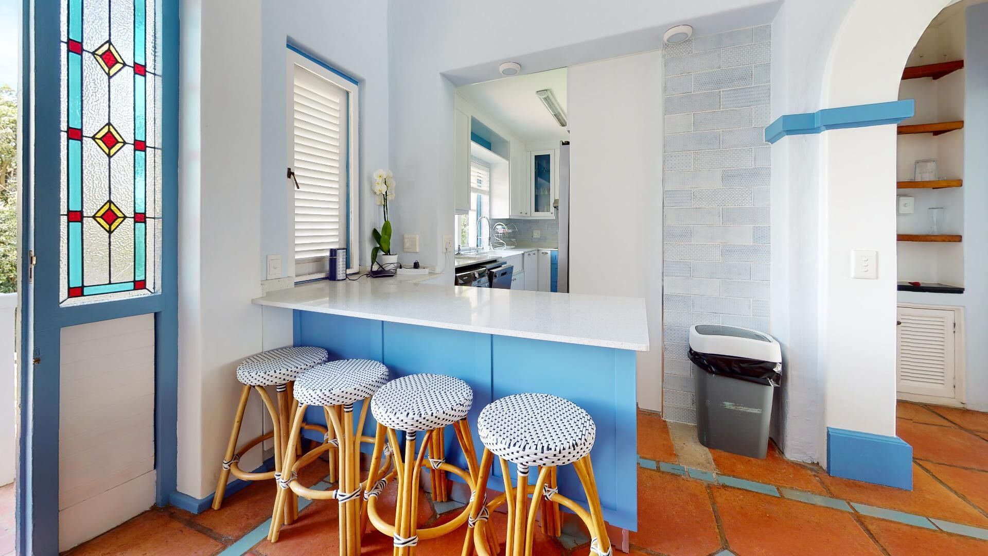 A kitchen with a white countertop, blue cabinets, and a white trash bin.