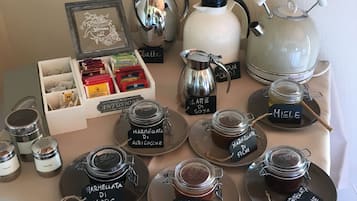 Una mesa con diferentes opciones de té y café, incluyendo una tetera blanca, un hervidor plateado y varios frascos de vidrio etiquetados con distintos tipos de mermelada.