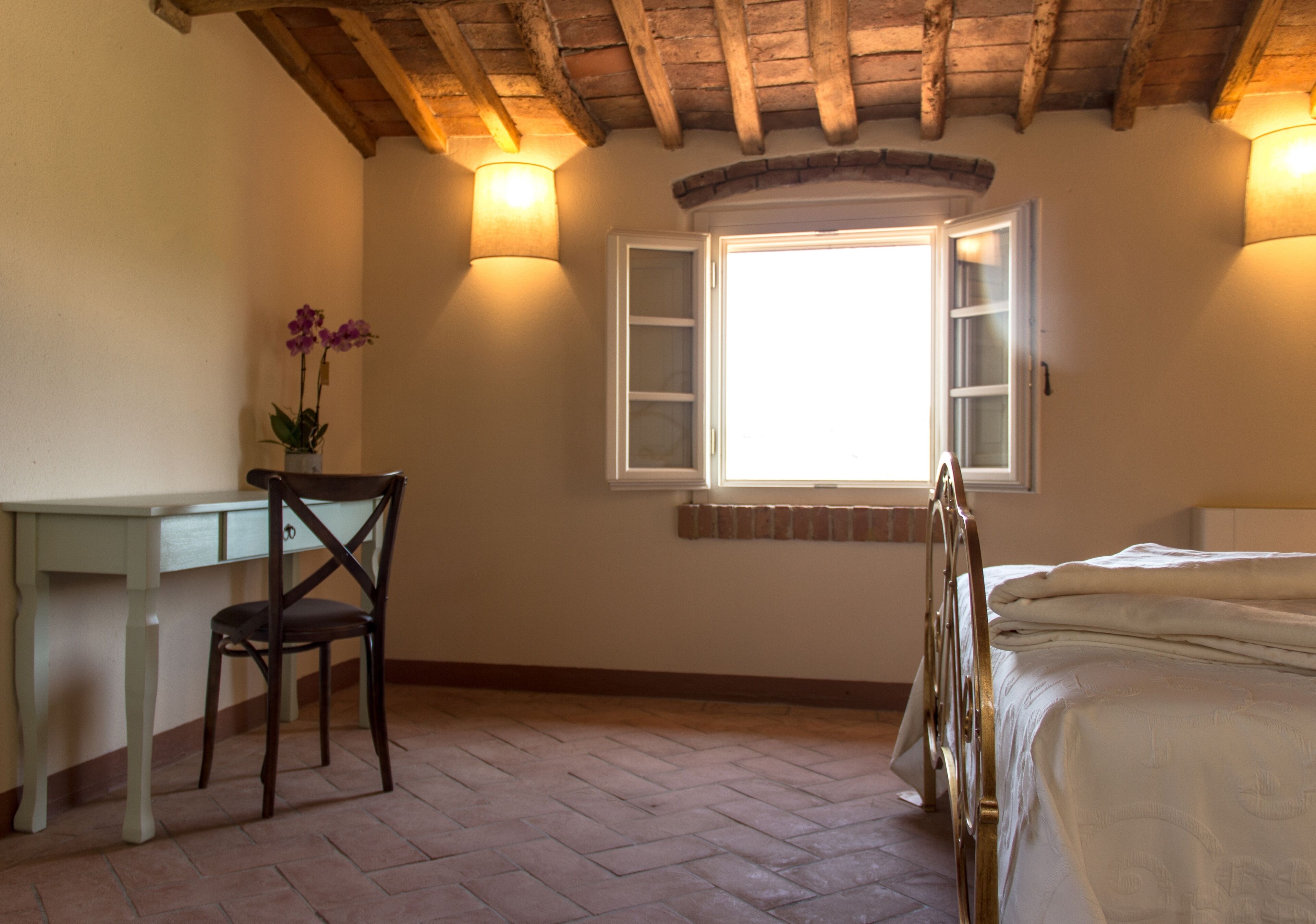 Ein Schlafzimmer mit Bett, Schreibtisch, Stuhl, Fenster und einer Wandleuchte.