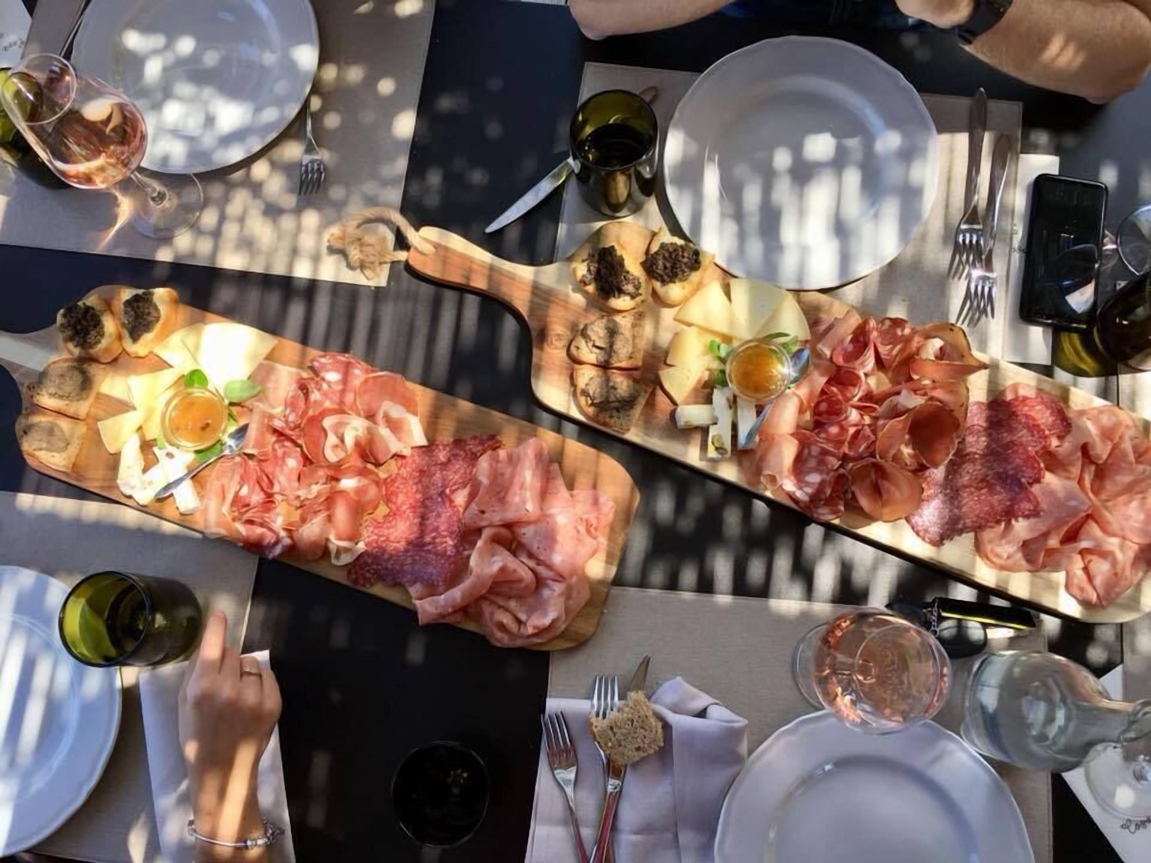 A dining table with a wooden board of assorted meats and cheeses, wine glasses, and cutlery.