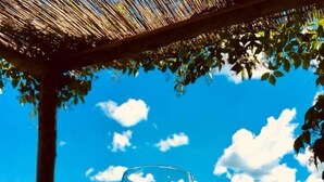 A group of people toasting with wine glasses under a thatched roof, with a clear blue sky and clouds in the background. - Locanda dell'Aioncino (Bibbona)