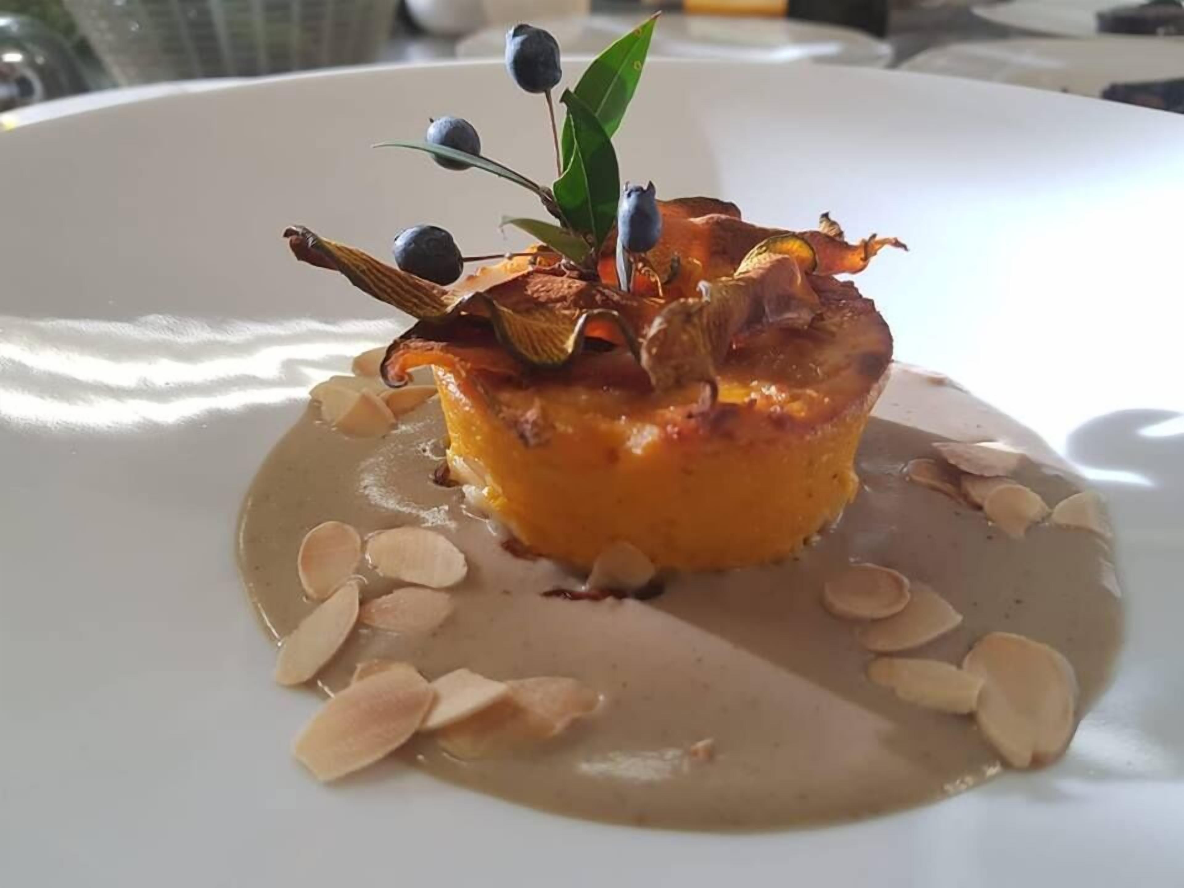 Jälkiruoka, jonka päällä on karamellisoitu kuorrute ja joka on koristeltu lehdillä ja marjoilla. Se tarjoillaan valkoiselta lautaselta, ja sen kanssa on manteliviipaleita.