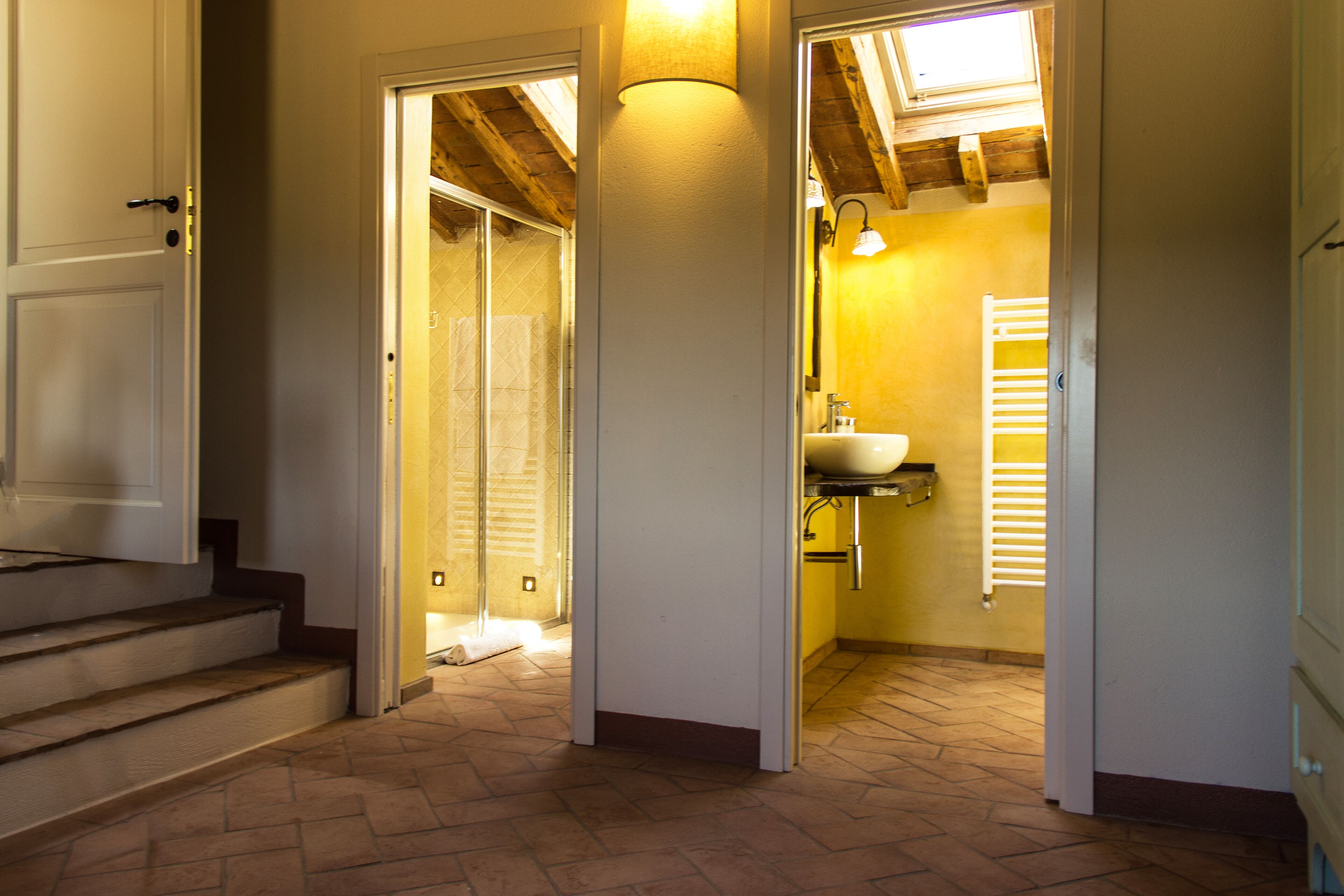 A hallway leading to a bathroom with a sink and towel rack, wooden stairs, and a tiled floor.
