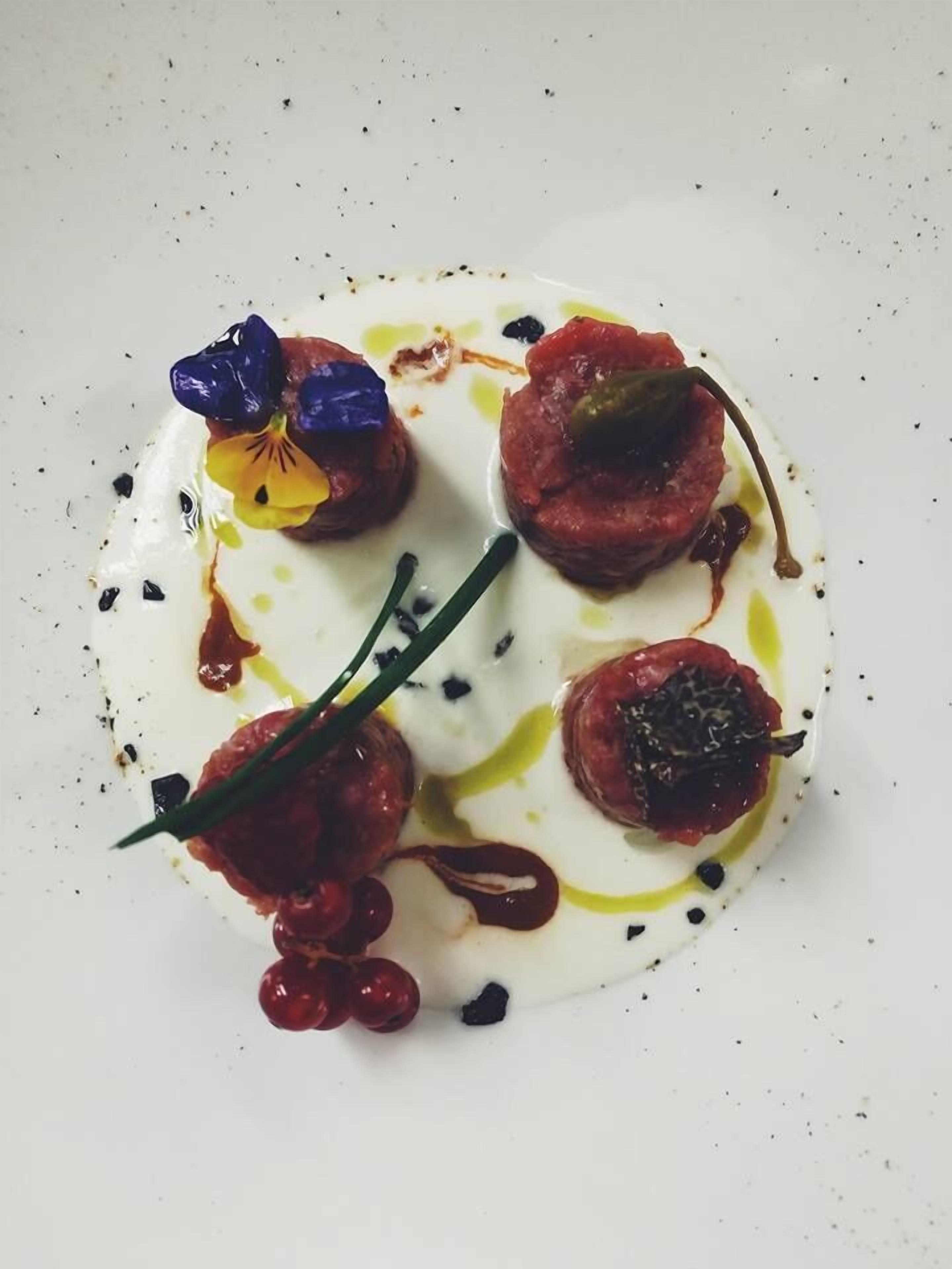 Un plato blanco con un guiso de comida, adornado con flores y bañado en salsa.