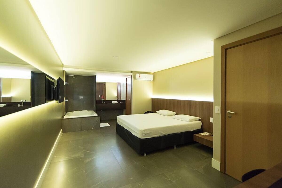 A modern hotel room with a large bed, a bedside table, a mirror, and a bathroom with a shower and sink.