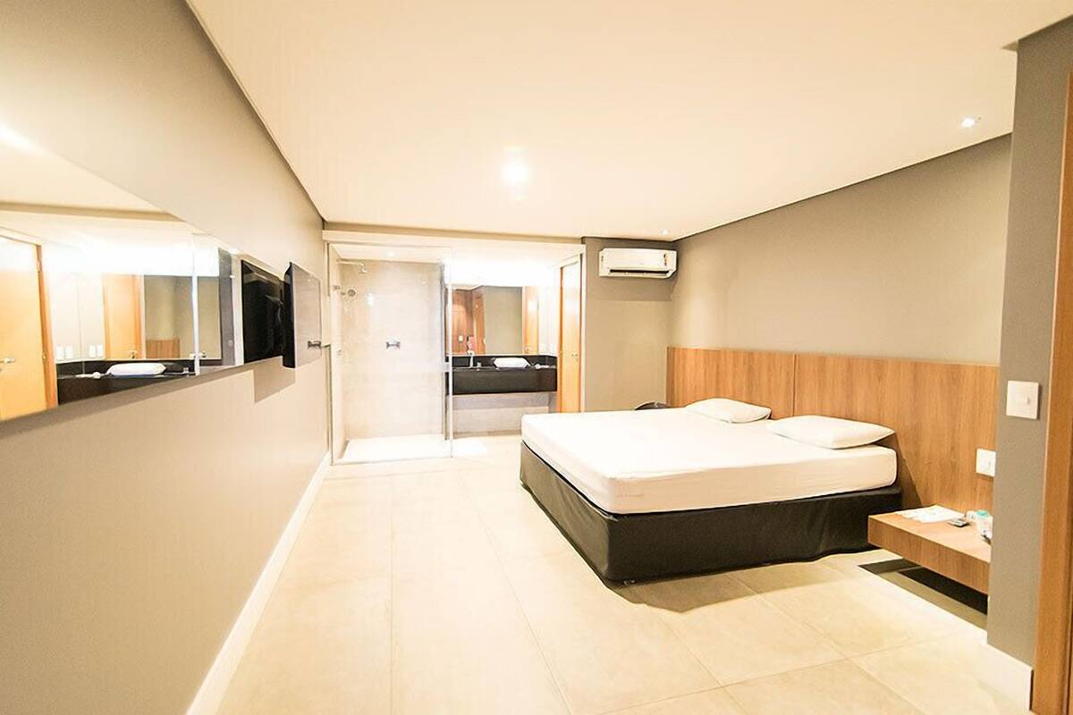 A modern hotel room with a large bed, a bedside table, a mirror, and a TV.