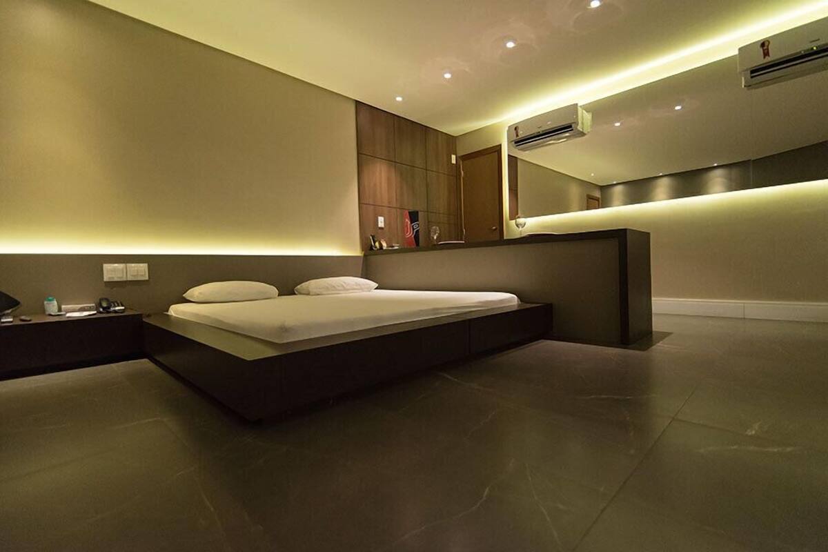 A modern bedroom with a large bed, bedside tables, a mirror, and an air conditioning unit.