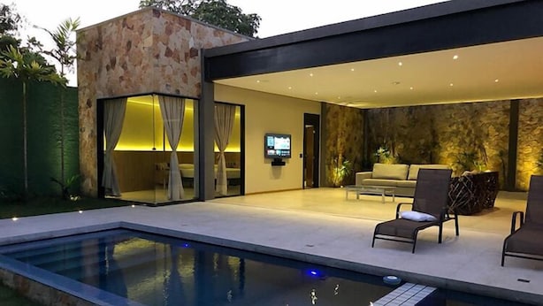 Un espacio exterior moderno con piscina, un muro de piedra y una zona de estar con televisor.