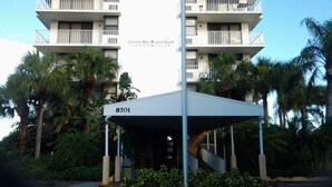 Un edificio de varios pisos con balcones, una entrada techada y palmeras.