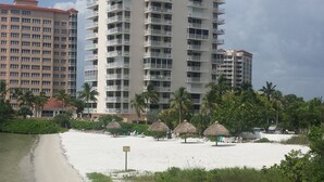 Un hotel frente a la playa con varios balcones, una playa de arena y palmeras.