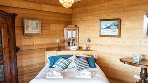 A wooden-paneled room with a bed, two lamps, a mirror, and framed pictures on the walls.