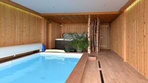 A modern indoor pool area with wooden walls and a bench along the pool.