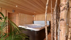 A wooden cabin with a hot tub, wooden walls, and birch trees.
