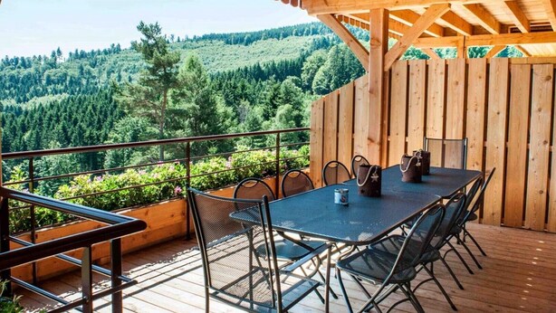 A wooden deck with a table and chairs, overlooking a forested valley.
