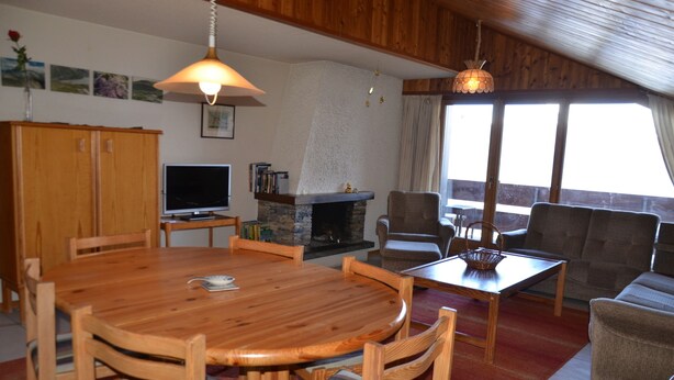 A cozy living room with a wooden dining table, chairs, a fireplace, a television, and a sofa. - Nice flat to rent in les Collons (Thyon-Les Collons)