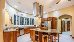 A spacious kitchen with wooden cabinets, a granite countertop, and a central island with stools. - Casa Tranquilidad | Jungle Villa | Infinity Pool + Jacuzzi | Manuel Antonio (Manuel Antonio)