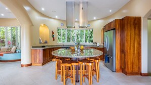 A modern kitchen with a central island, wooden bar stools, and a stainless steel refrigerator. - Casa Tranquilidad | Jungle Villa | Infinity Pool + Jacuzzi | Manuel Antonio (Manuel Antonio)