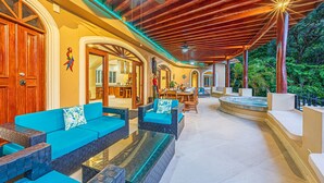 A spacious outdoor lounge area with wooden ceiling beams, blue cushioned seating, and a glass-top table. - Casa Tranquilidad | Jungle Villa | Infinity Pool + Jacuzzi | Manuel Antonio (Manuel Antonio)