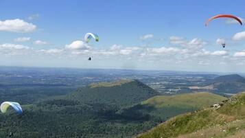 Un paysage montagneux où l’on peut apercevoir de nombreux parapentes dans le ciel.