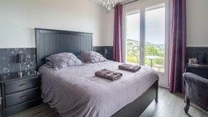 Un dormitorio con una cama grande, una mesita de noche, un aparador, una silla y vistas al exterior.