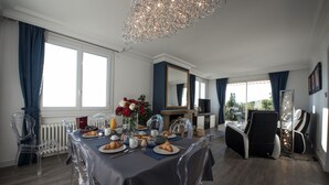 Comedor con una mesa dispuesta para el desayuno, sillas traslúcidas, una araña de cristal y vistas al exterior.
