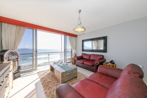 A living room with a large window overlooking the ocean, a red leather sofa, a wooden coffee table, and a ceiling light.