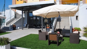 Entrada de un hotel con una zona de estar techada al aire libre, una escalera y un césped bien cuidado.