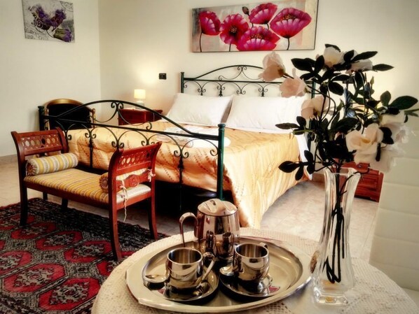 A hotel room with a bed, two chairs, a coffee table with tea cups, a vase with flowers, and a painting on the wall. - B&B Main Street (Reggio Calabria)