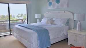 A bedroom with a large bed, two bedside lamps, a nightstand, and a view of the outdoors through a sliding glass door. - Beautiful Oceanfront Penthouse ~ Incredible Views ~ Pool (Saint Augustine)