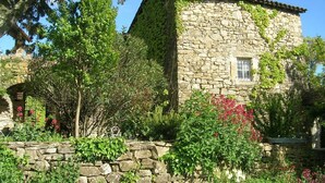A stone building with a tiled roof, surrounded by lush greenery and flowering plants. - Charming accommodation in a large 16th century building with swimming pool and garden (Vesseaux)