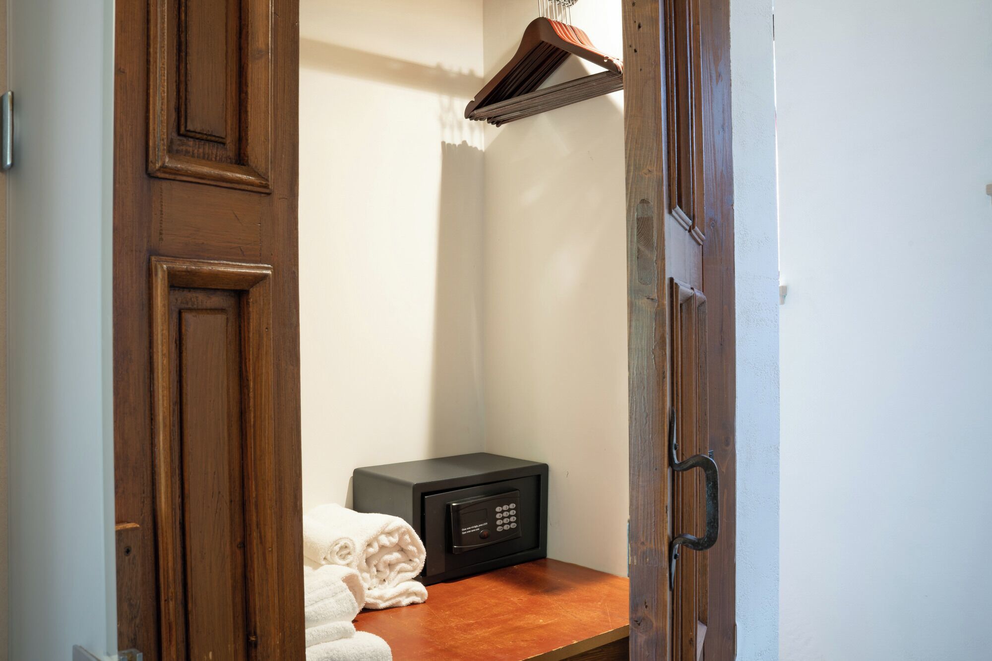 A wooden wardrobe with a black appliance, possibly a microwave, and a folded white towel on a wooden shelf.