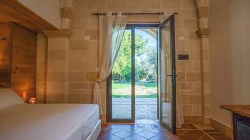 A bedroom with a bed, a window with curtains, and a view of a garden through an open door.