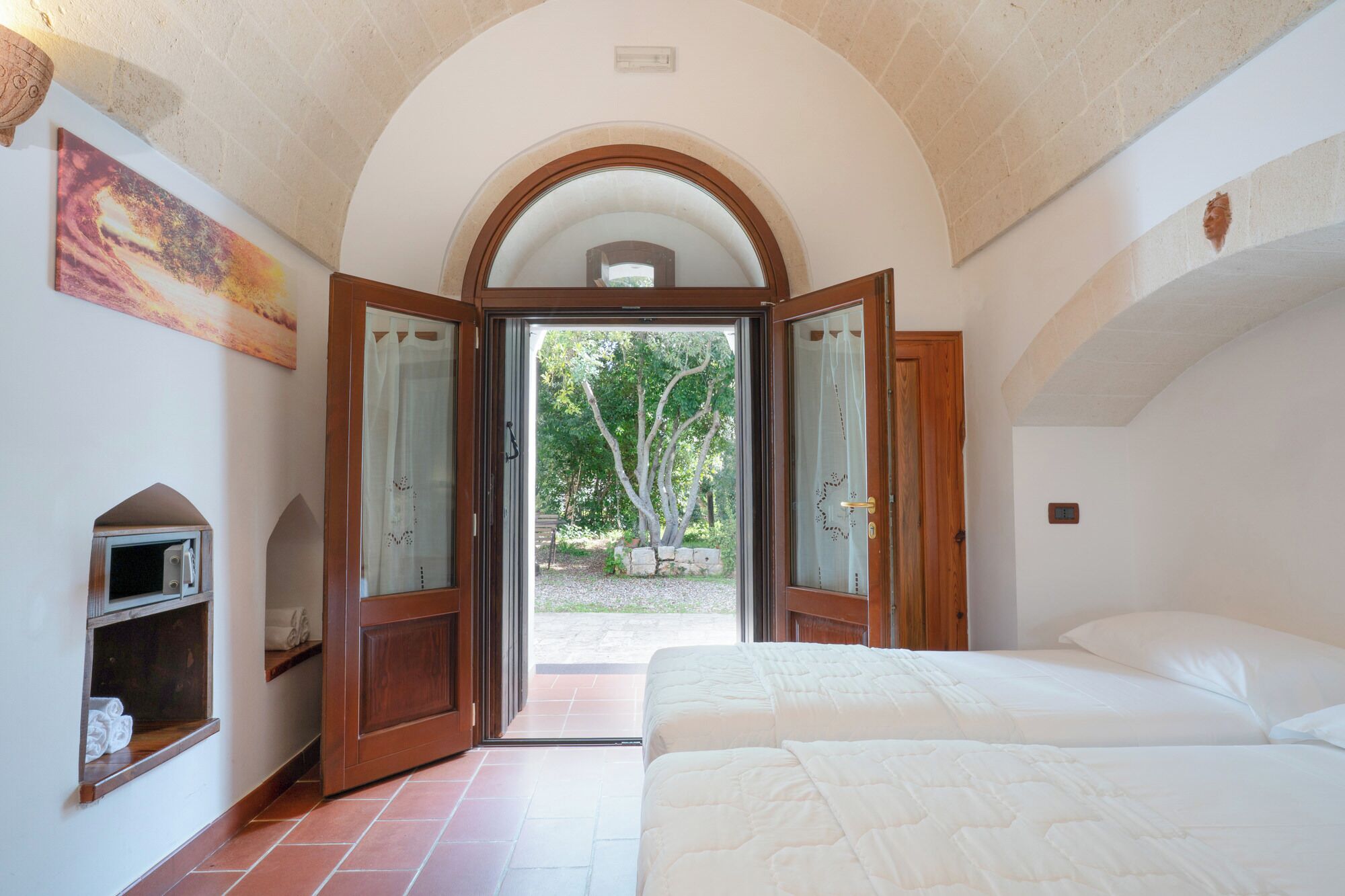 Un dormitorio con una cama grande, una puerta de madera que da a un jardín y un pequeño estante con toallas.