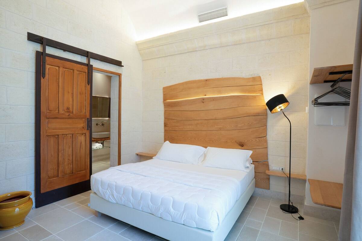 Ein Schlafzimmer mit einem hölzernen Kopfteil, einem weißen Bett, einem Nachttisch, einer Nachttischlampe und einem Holzschrank mit Spiegel.