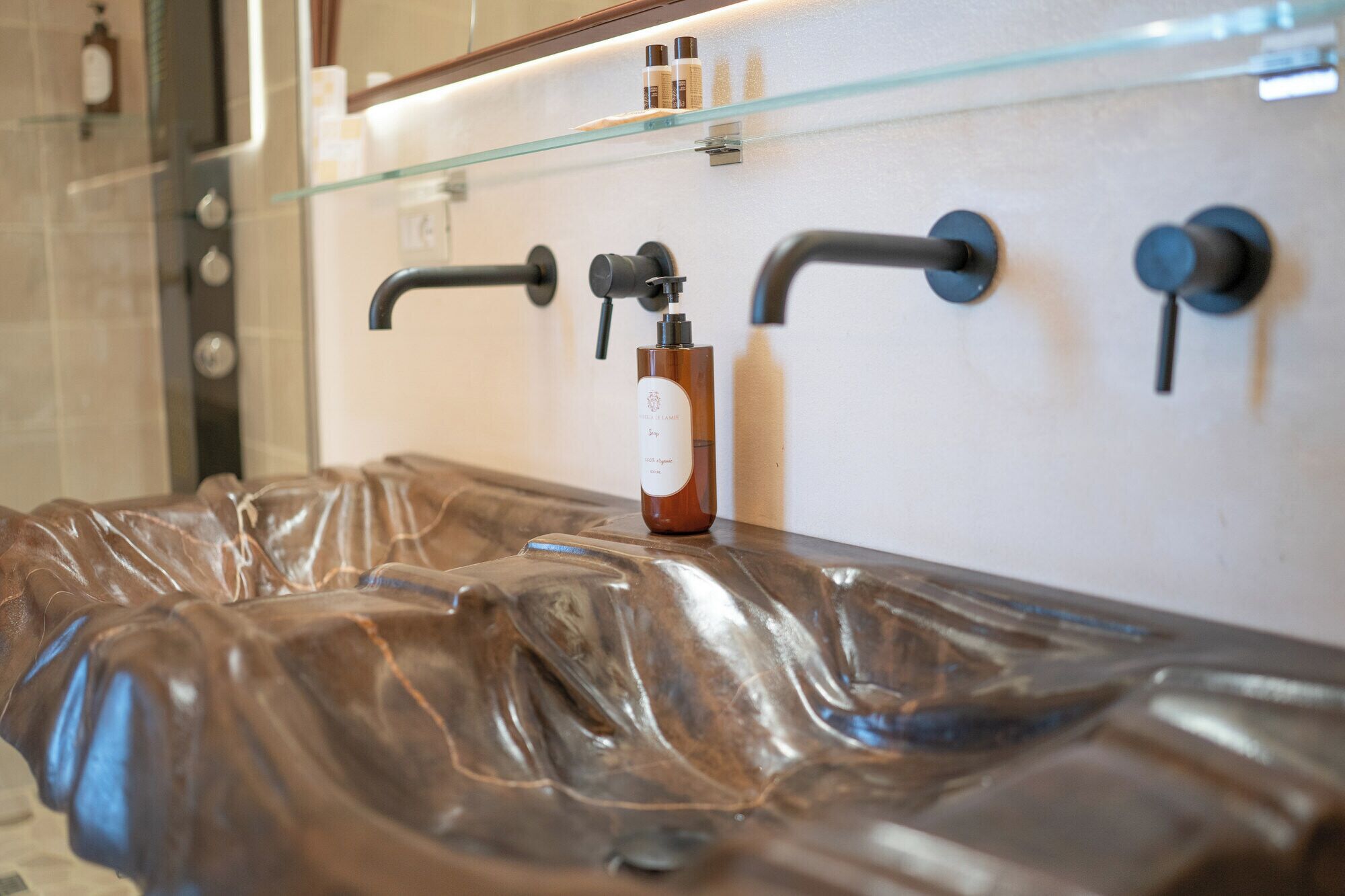 Un baño con diseño moderno, que incluye un estante de vidrio sobre un lavamanos y una botella de jabón en la encimera.