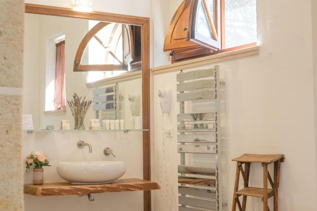 Un baño con tocador de madera, un lavabo blanco, un espejo y una ventana con marco de madera.