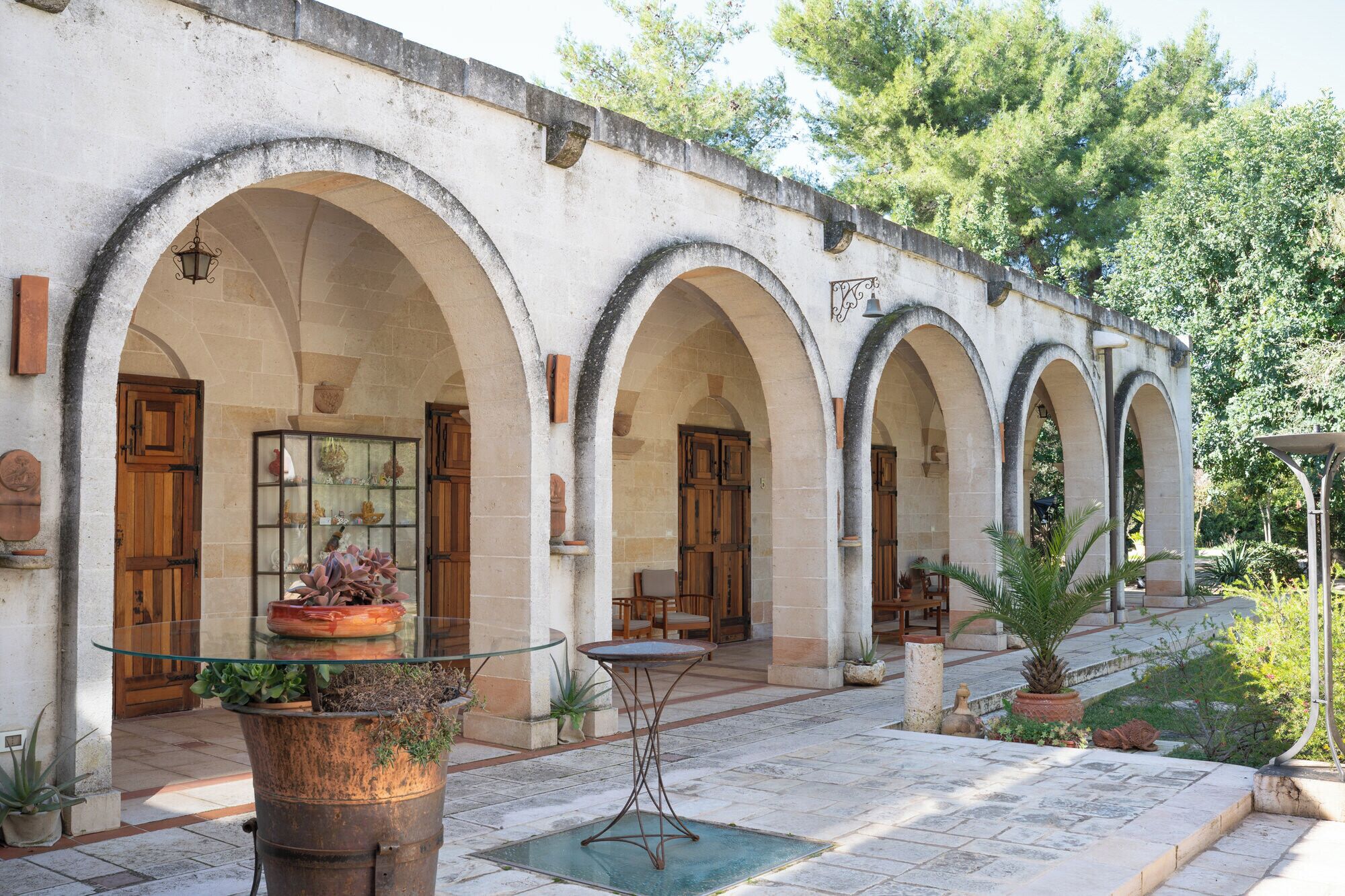 A building with multiple arched doorways, a glass table, and potted plants.