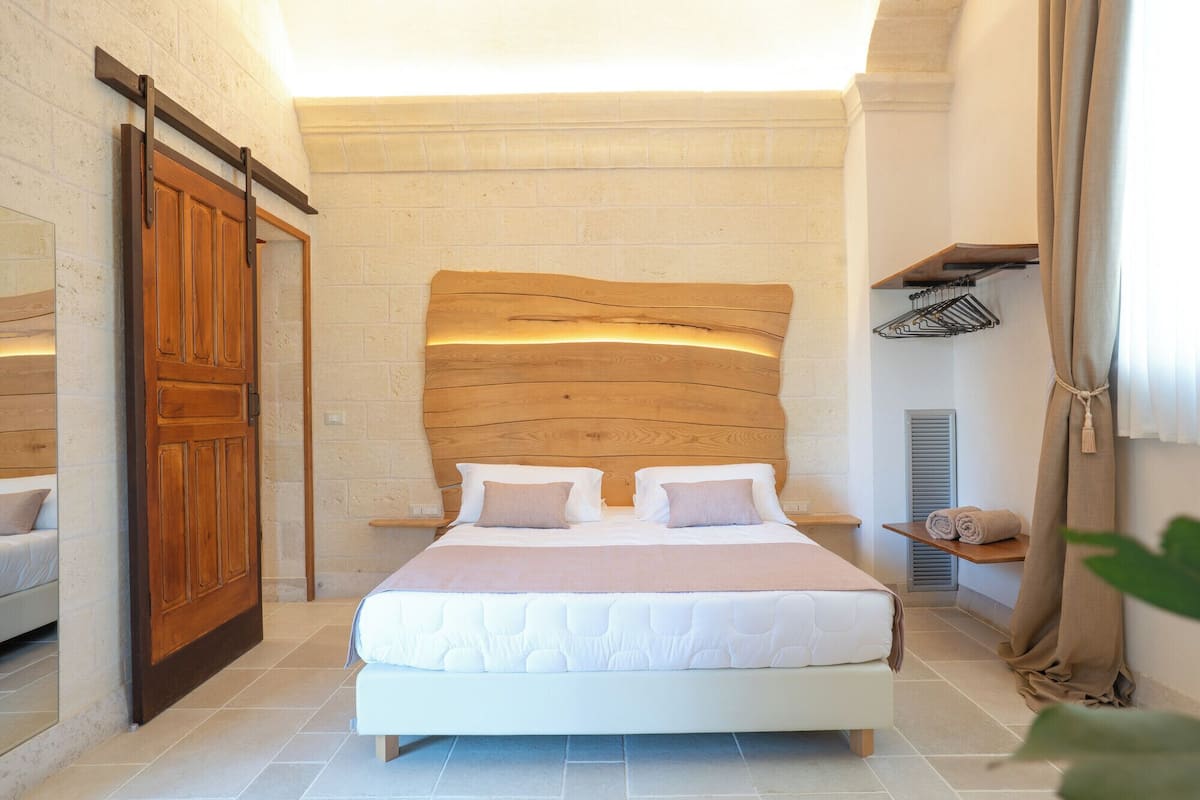Ein Schlafzimmer mit einem hölzernen Kopfende, einem großen Bett mit weißer Bettwäsche, einem Holzschrank und einem kleinen Regal mit Handtüchern.