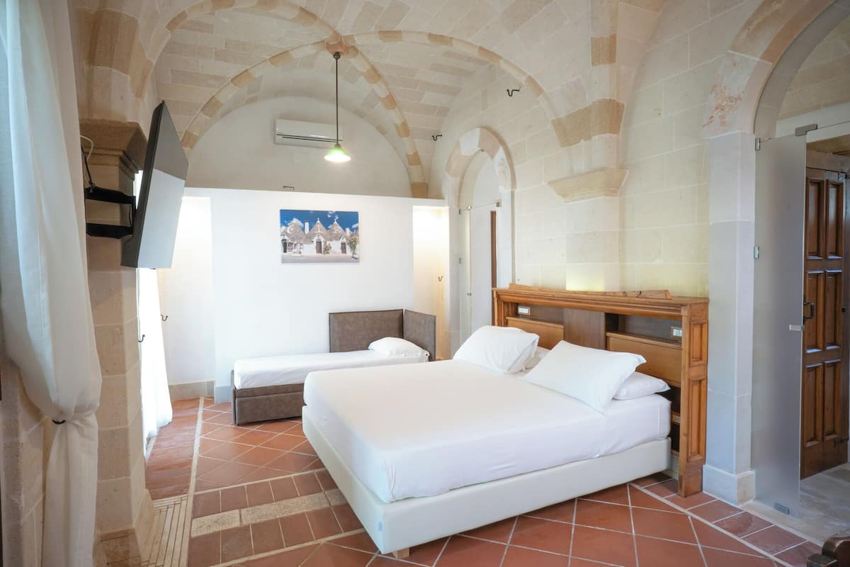Ein Schlafzimmer mit einem großen Bett, einem Schreibtisch und einem Stuhl. An der Wand hängt ein Gemälde, und es gibt eine Klimaanlage.