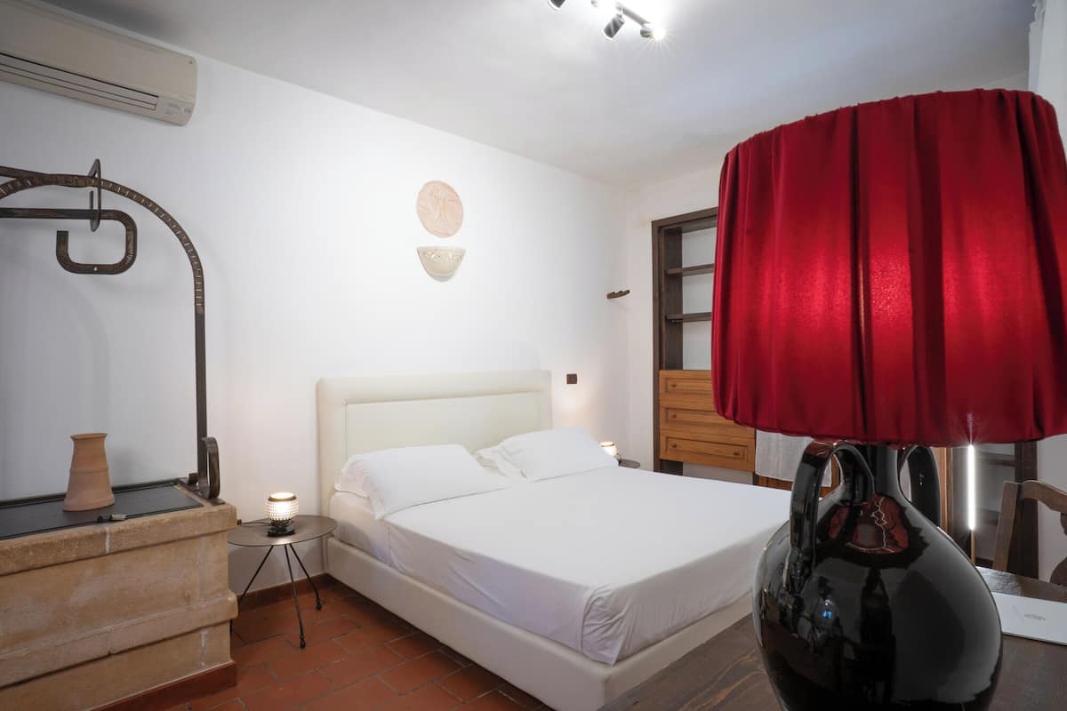 Ein Schlafzimmer mit einem Bett, einem Nachttisch, einer roten Lampe, einem an der Wand befestigten Regal und einem roten Vorhang.