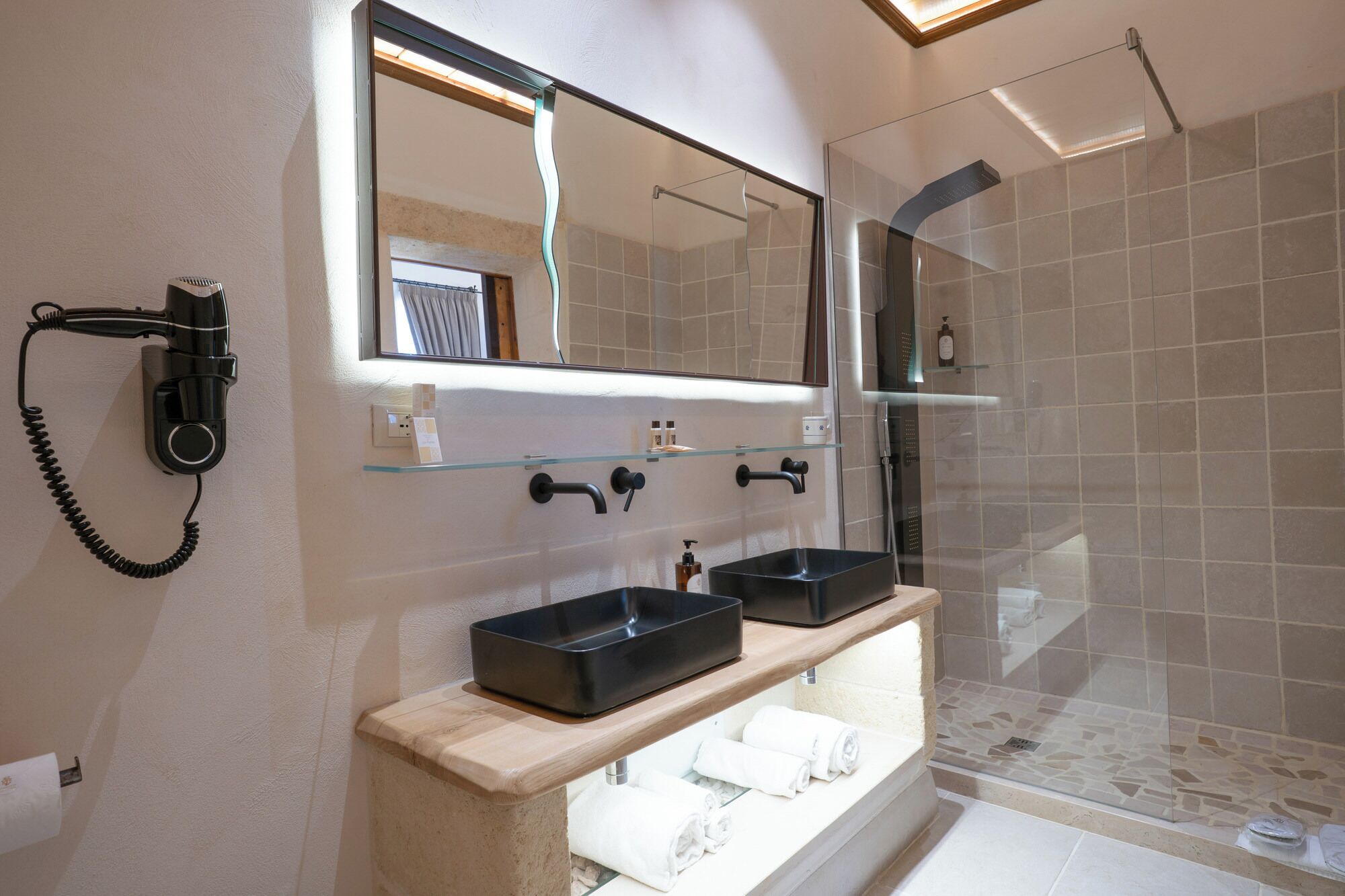 Un baño moderno con lavamanos doble, secador de pelo, cabina de ducha de vidrio y espejo sobre el lavamanos.