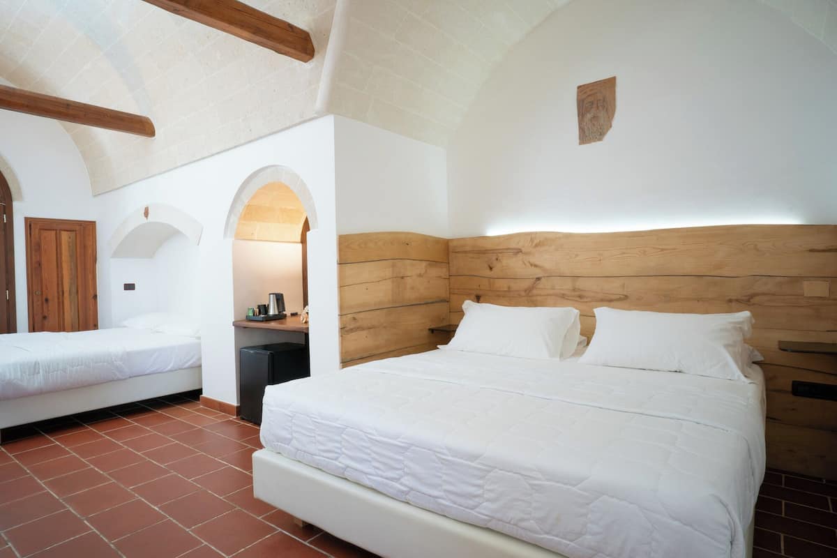 Ein Schlafzimmer mit einem großen Bett, einem Einzelbett, einem Schreibtisch mit Kaffeemaschine und einem Holzkopfende.