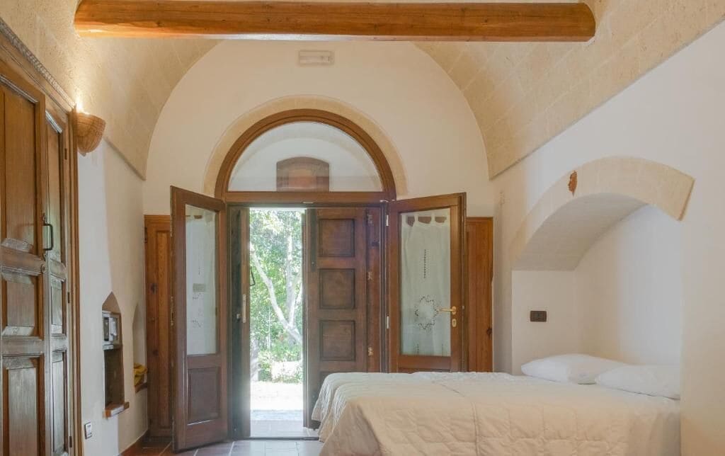A bedroom with a bed, an arched doorway, and a view of the outdoors.