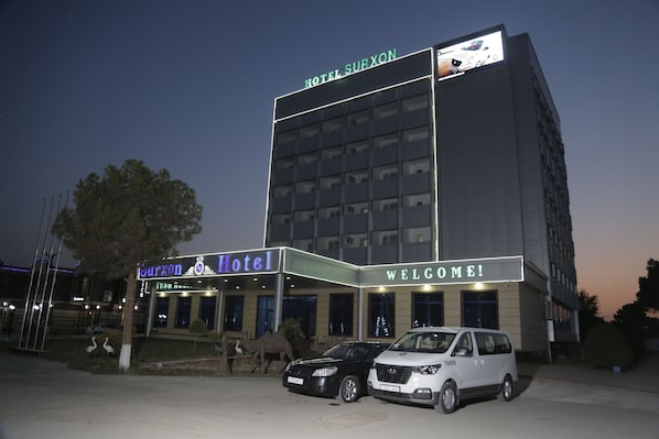 A hotel with a 'Hotel Surxon' sign, a 'Welcome!' sign, and two cars parked in front.