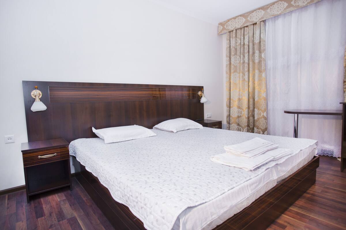 A neatly made bed with white linens, a wooden headboard, and two bedside lamps.