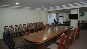 Uma sala de conferências com uma longa mesa de madeira rodeada por cadeiras, uma poltrona de couro preto e um quadro branco.
