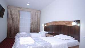 Quarto de hotel com duas camas, cabeceira de madeira e uma janela grande com cortinas.
